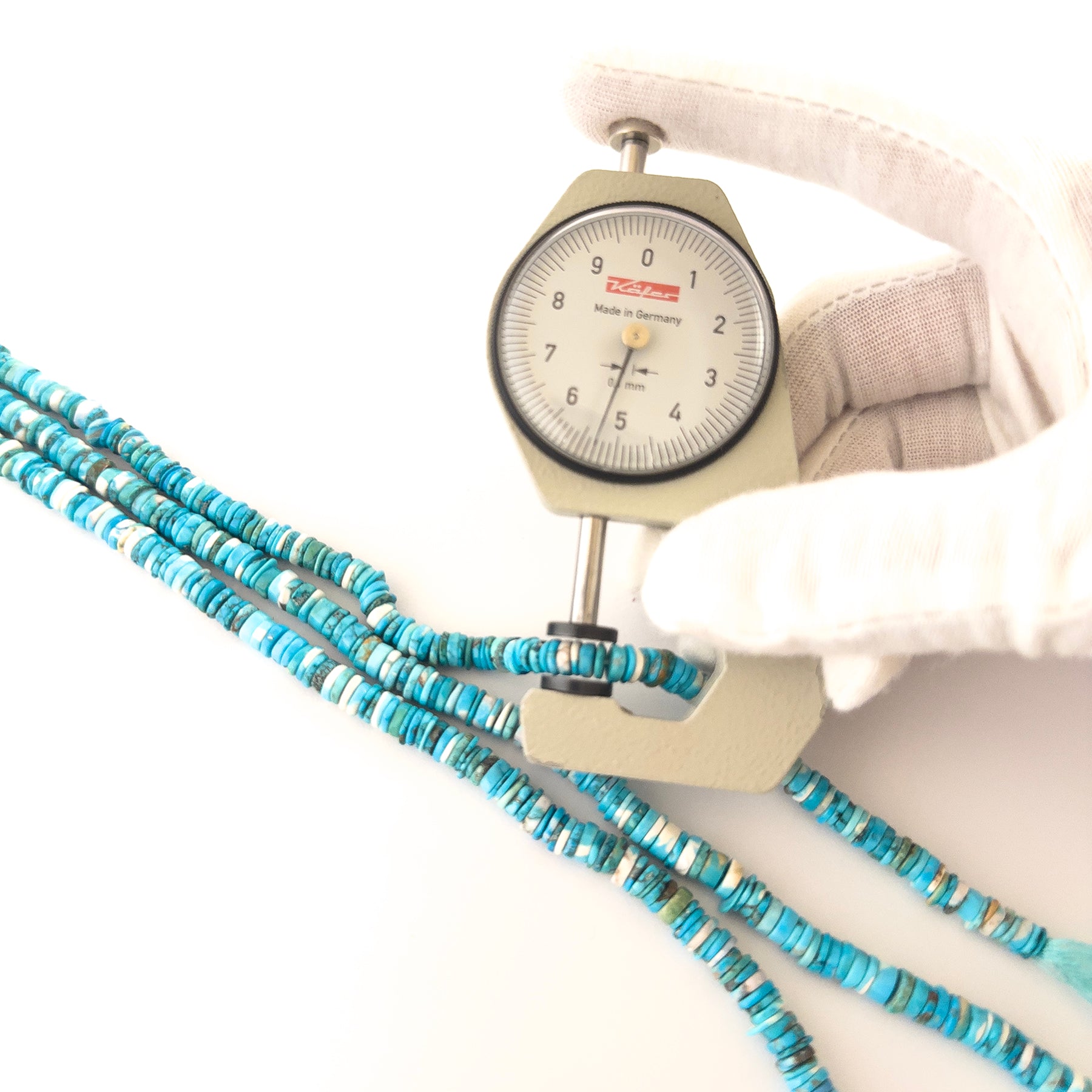 A dial gauge measures the Howlite Turquoise smooth wheel heishi 5–5.5mm gemstone.