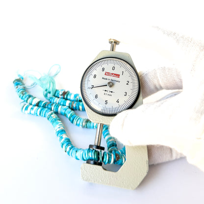 A dial gauge measures the Howlite Turquoise smooth wheel heishi 6.5–7mm gemstone.
