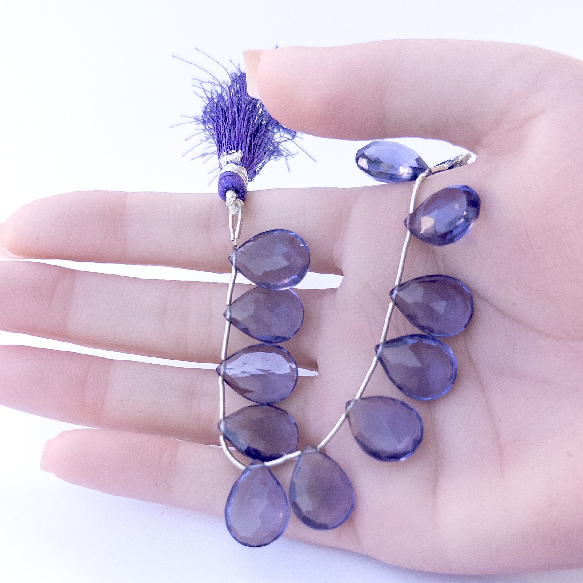 A person holds delicate pieces of Hydro beads, showcasing their faceted briolette design.