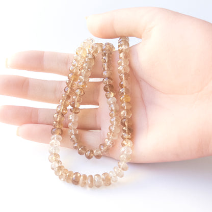 A person holds delicate strands of Imperial Topaz beads, showcasing their faceted rondelle design.