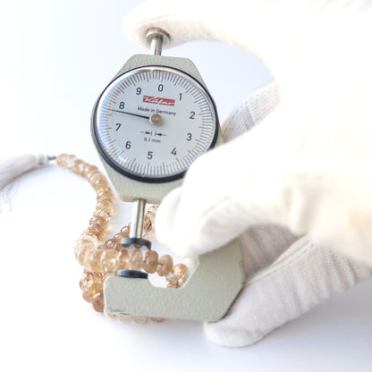 A dial gauge measures the Imperial Topaz faceted rondelle 7–7.5mm gemstone.