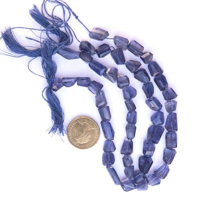 A coin is placed near delicate strands of Iolite beads for scale.