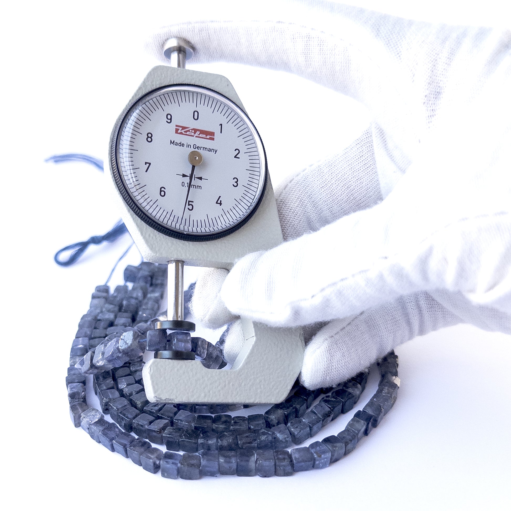 A dial gauge measures the Iolite smooth cube 4.5–5.3mm gemstone.