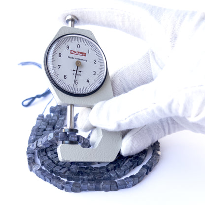 A dial gauge measures the Iolite smooth cube 4.5–5.3mm gemstone.