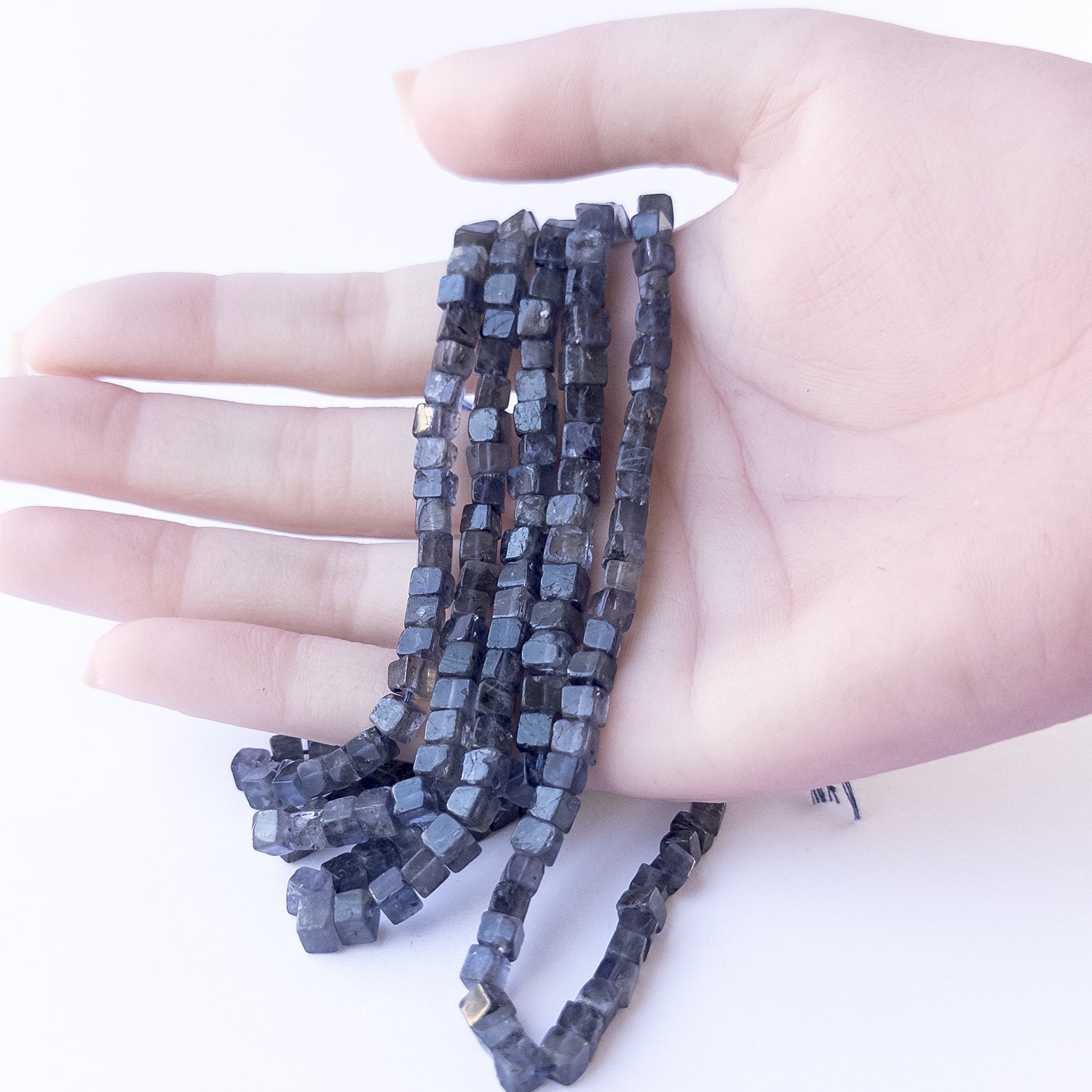 A person holds delicate strands of Iolite beads, showcasing their smooth cube design.