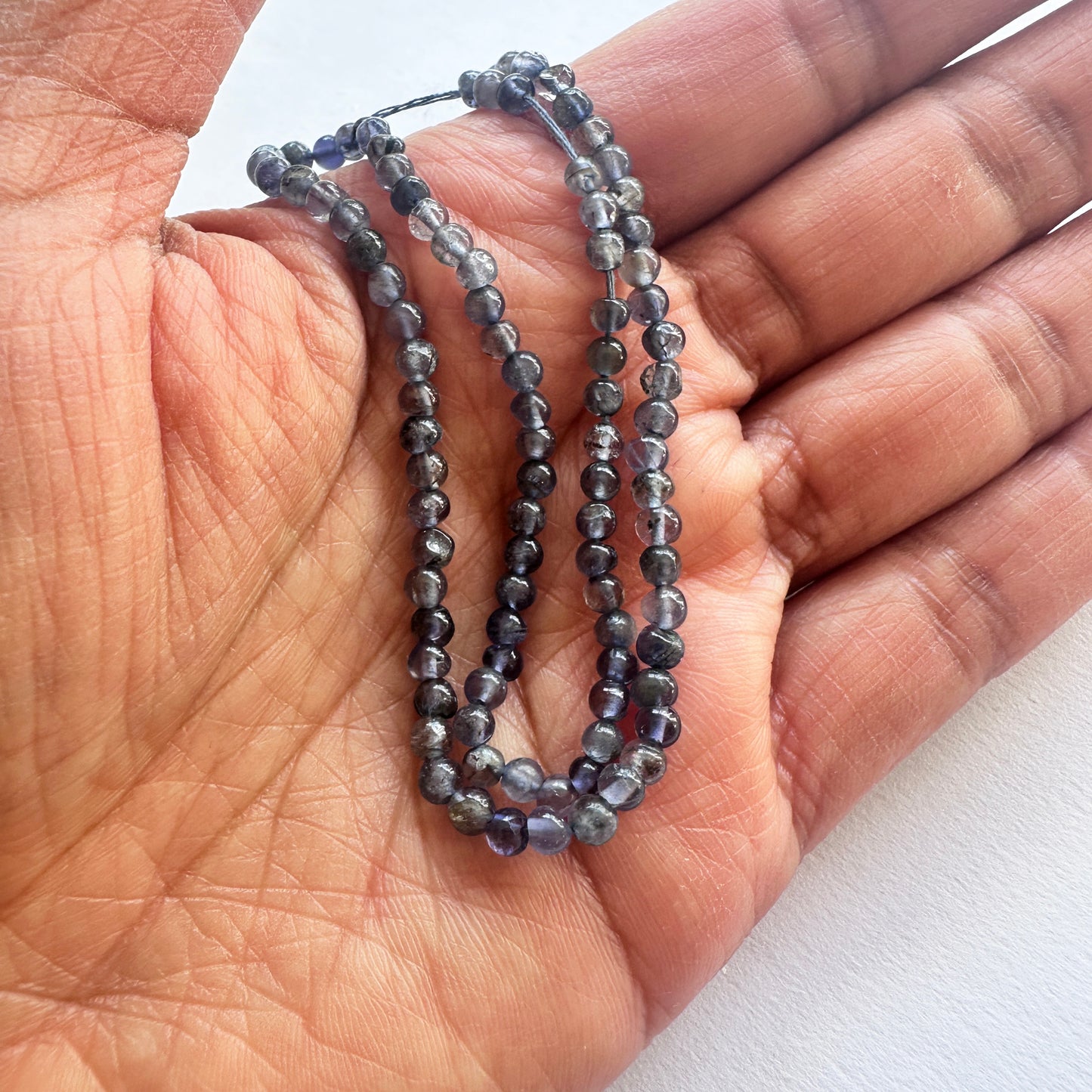 A person holds delicate strands of Iolite beads, showcasing their smooth design.