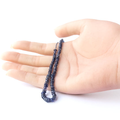 A person holds delicate strands of Iolite beads, showcasing their smooth wheel design.