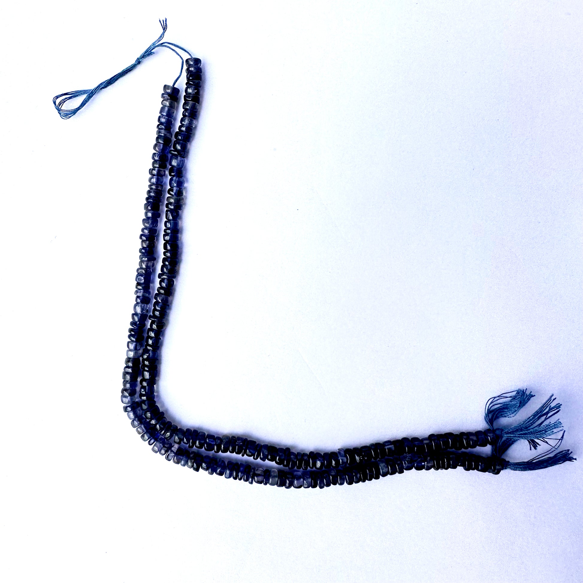 Close-up of Iolite gemstone beads arranged in a 21cm strand with smooth wheel cut.