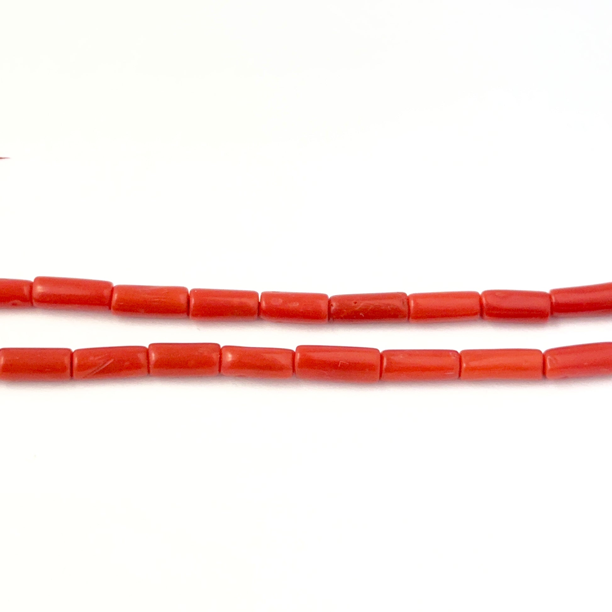 Italian Coral smooth cylinder beads displayed in a pack of five to highlight their warm tone and even sizing.