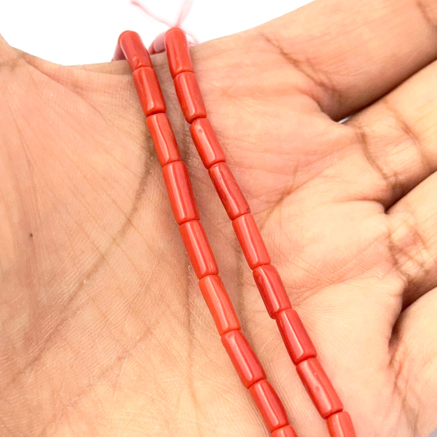 A person holds delicate strands of Italian Coral beads, showcasing their smooth design.