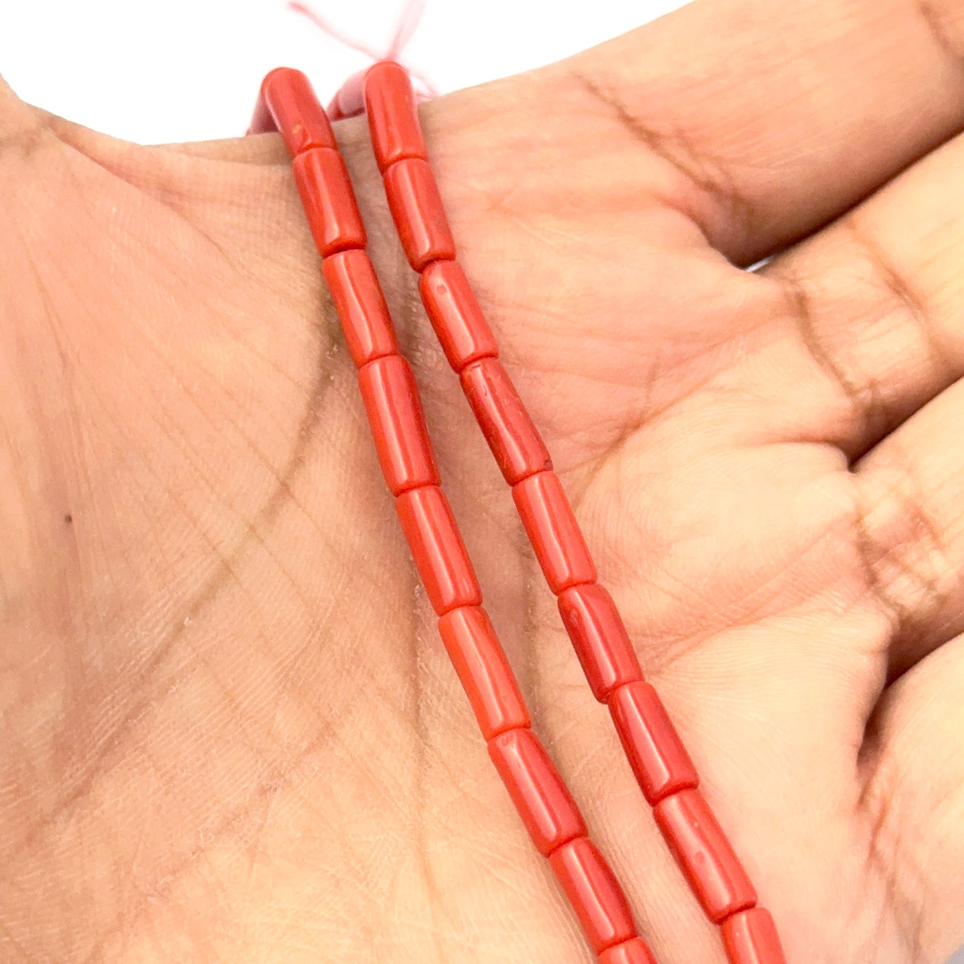 A person holds delicate strands of Italian Coral beads, showcasing their smooth design.