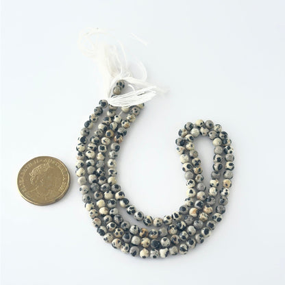 A coin is placed near delicate strands of Jasper beads for scale.