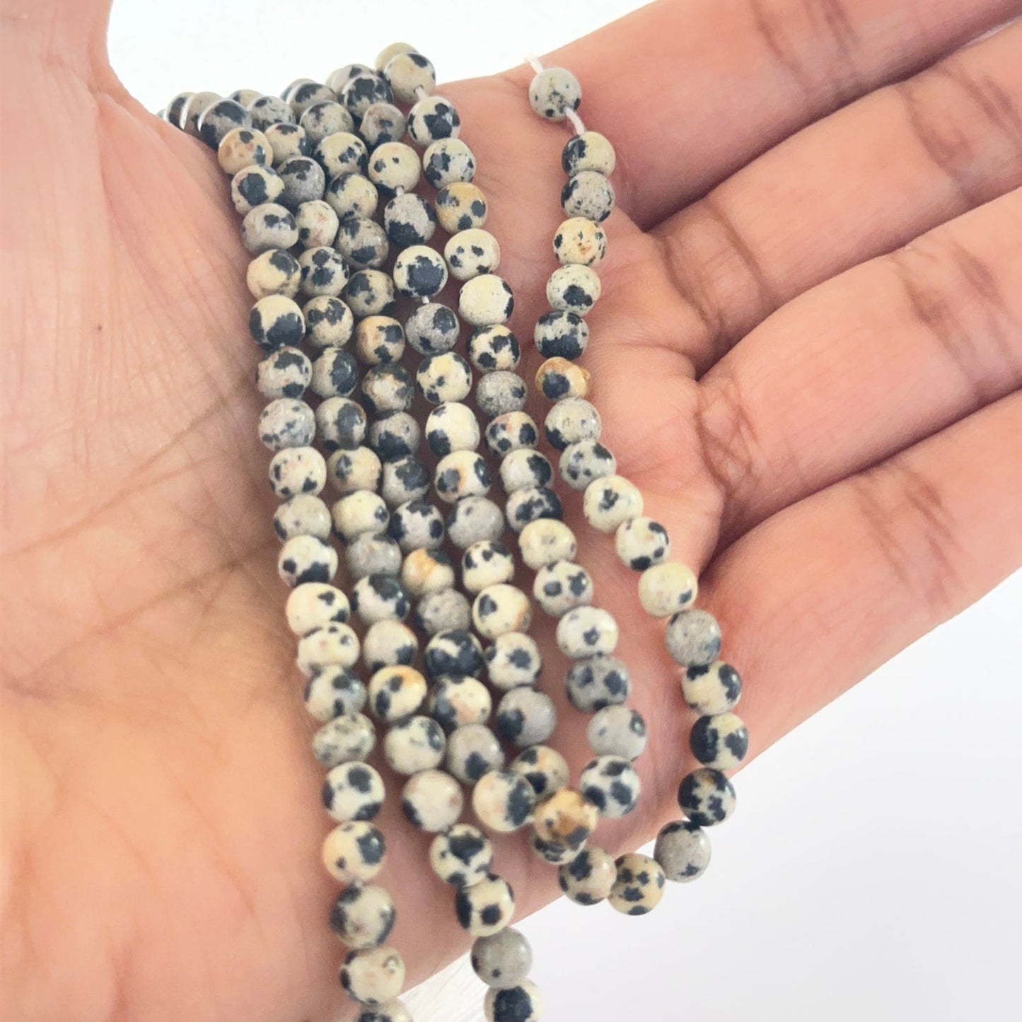 A person holds delicate strands of Jasper beads, showcasing their smooth round design.