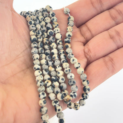 A person holds delicate strands of Jasper beads, showcasing their smooth round design.