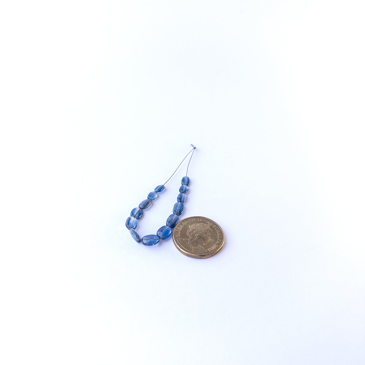 A coin is placed near delicate pieces of Kyanite beads for scale.