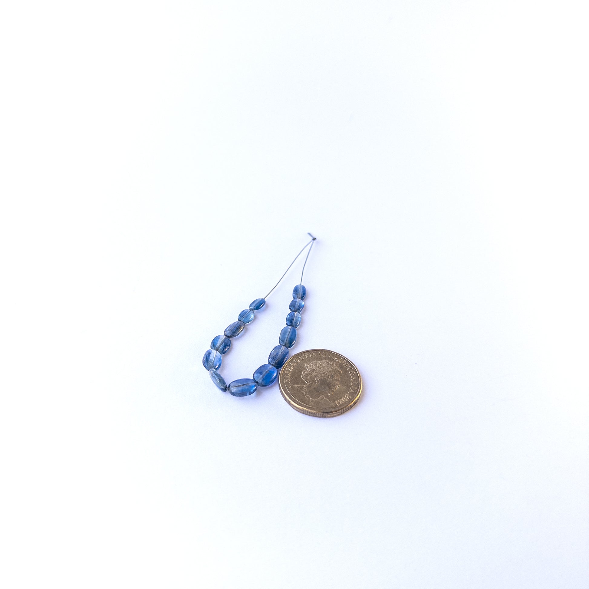 A coin is placed near delicate pieces of Kyanite beads for scale.