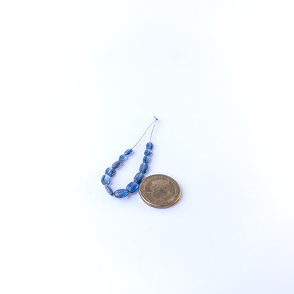 A coin is placed near delicate pieces of Kyanite beads for scale.