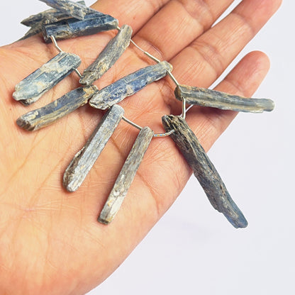 A person holds delicate strands of kyanite rough beads, showcasing their smooth design.