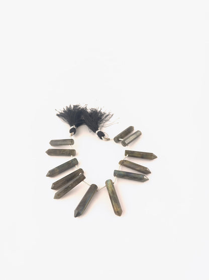 Labradorite faceted pencil briolette beads sized 6–7mm arranged as an 11‑piece set, showing grey‑blue body colour with flashes of labradorescence and sharp faceting.