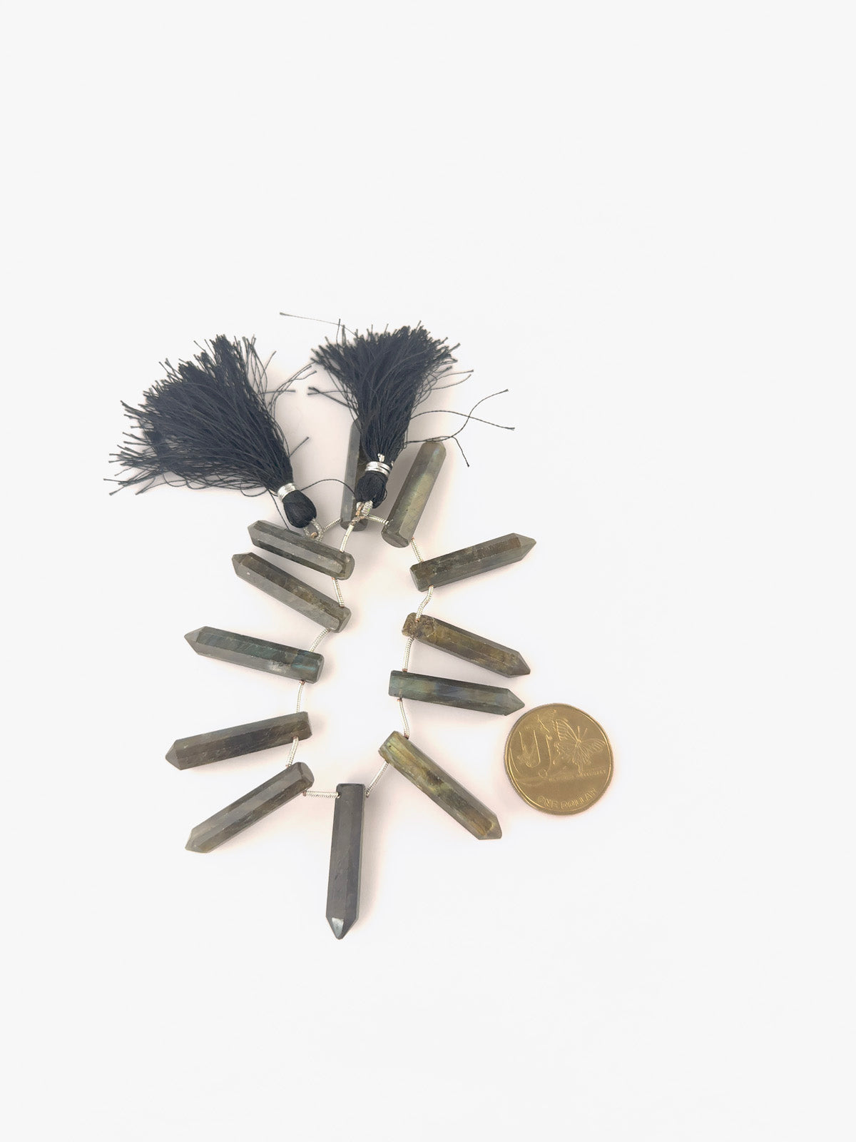 A coin is placed near Labradorite pencil briolette beads.