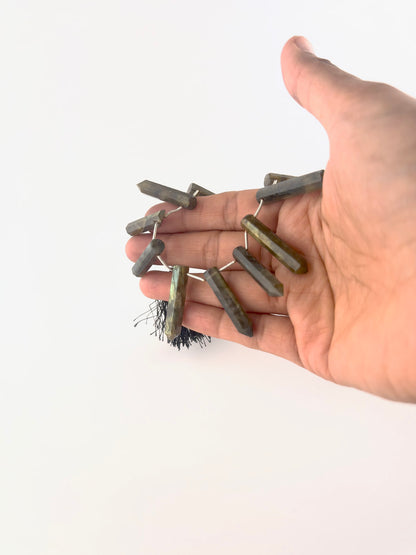 A person holds Labradorite pencil briolette beads, showing their faceted elongated design and colour play.