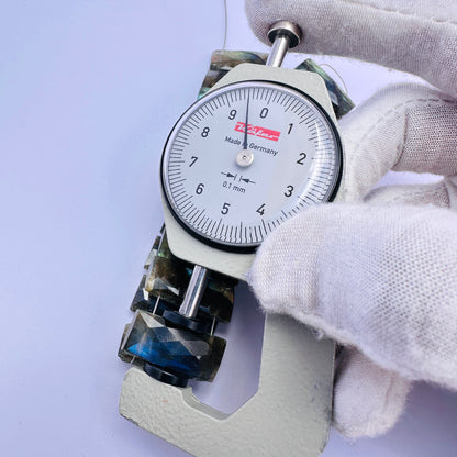 A dial gauge measures the Labradorite faceted rectangle 21mm × 9mm gemstone.