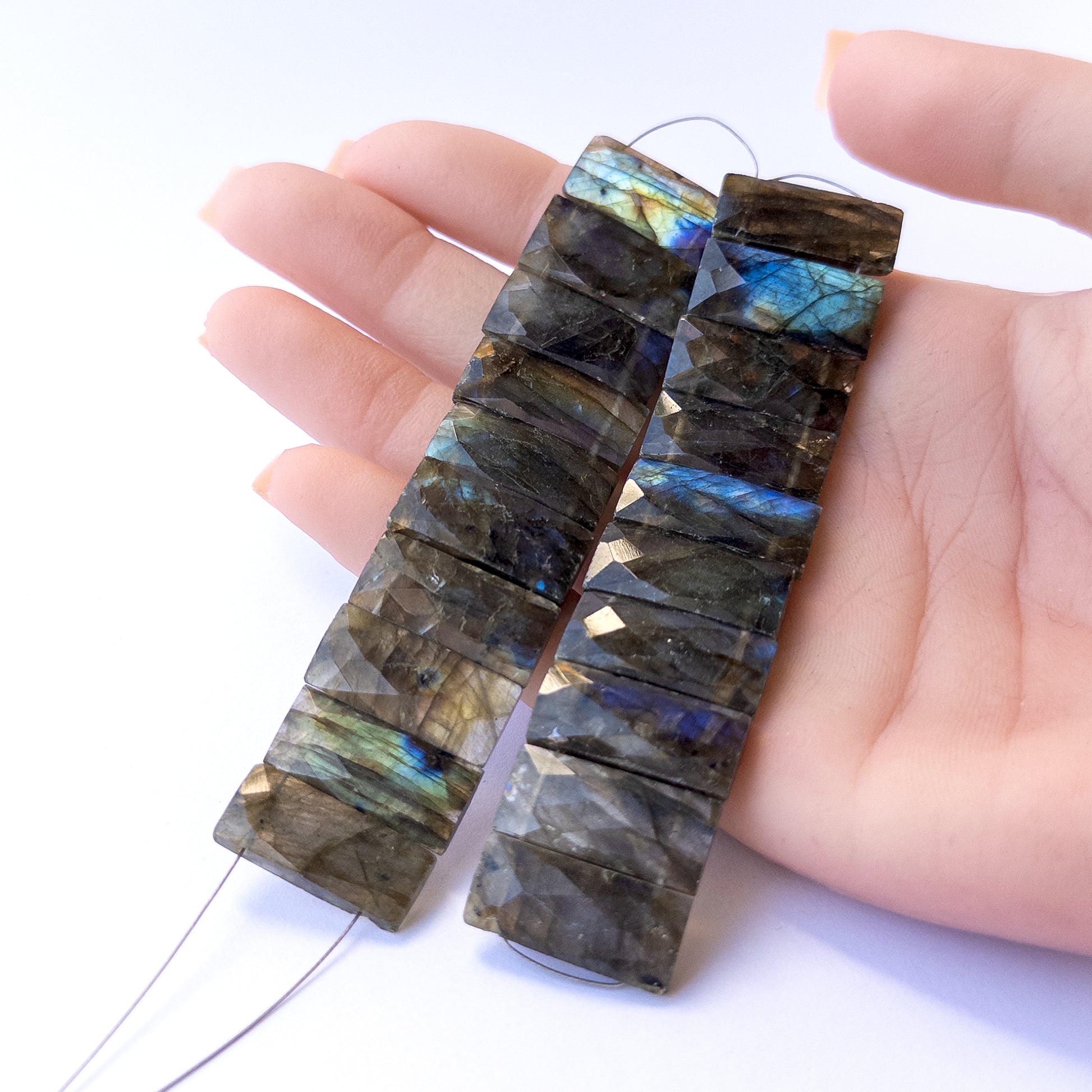 A person holds delicate pieces of Labradorite beads, showcasing their faceted rectangle design.