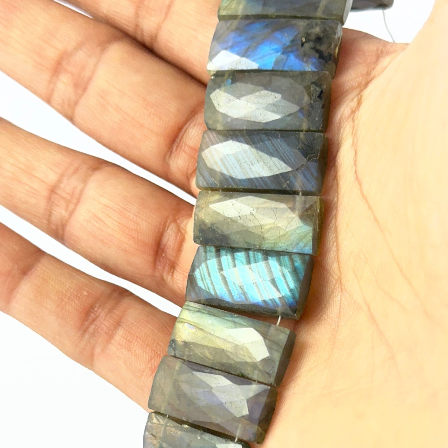 A person holds delicate strands of Labradorite beads, showcasing their faceted rectangle design.