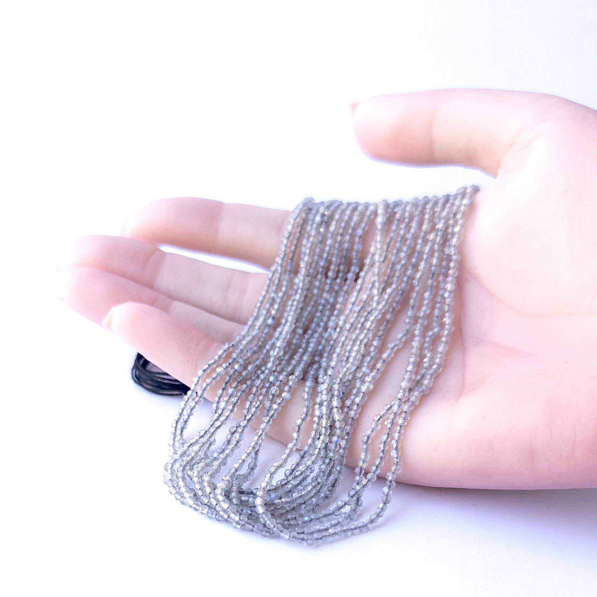 A person holds delicate strands of Labradorite beads, showcasing their faceted rondelle design.