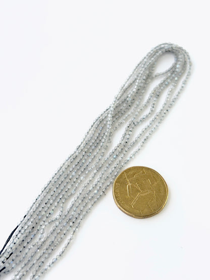 A coin is placed near delicate strands of Labradorite beads for scale.