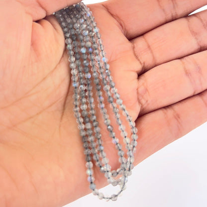 A person holds delicate strands of Labradorite beads, showcasing their faceted rondelle design.