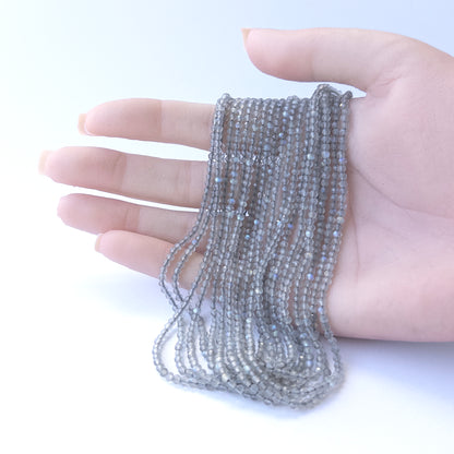 A person holds delicate strands of Labradorite beads, showcasing their Faceted Rondelle design.