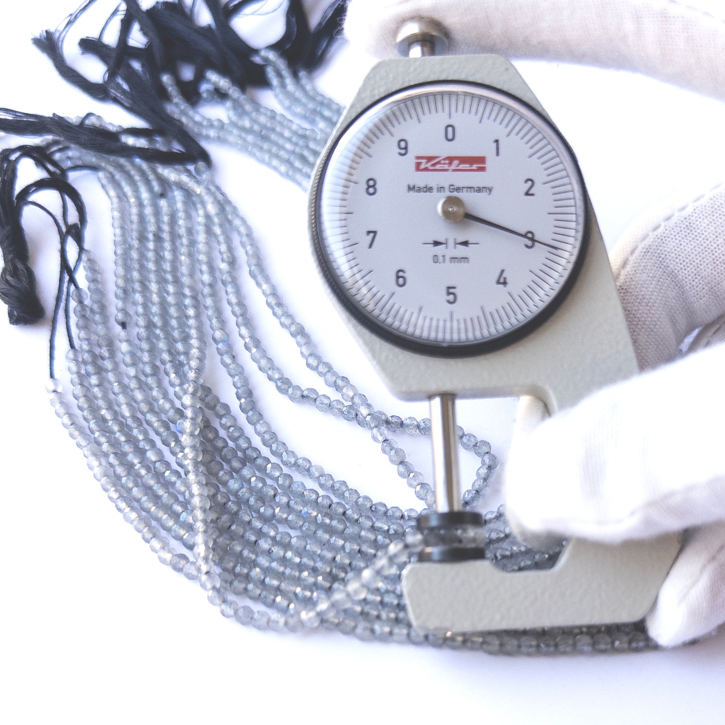A dial gauge measures the Labradorite faceted rondelle 3.1–3.2mm gemstone.