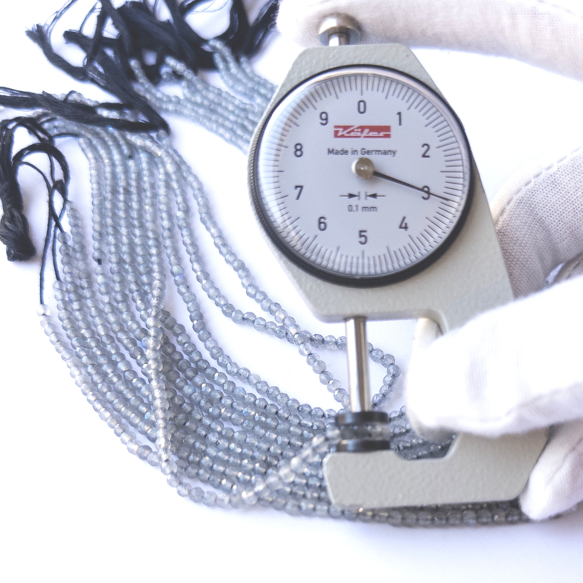 A dial gauge measures the Labradorite faceted rondelle 3.1–3.2mm gemstone.