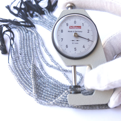 A dial gauge measures the Labradorite faceted rondelle 3.1–3.2mm gemstone.