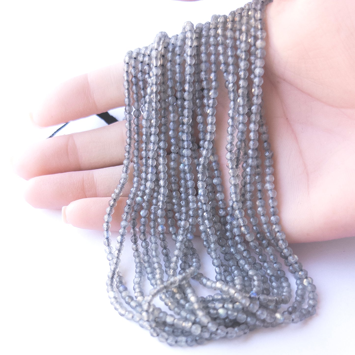 A person holds delicate strands of Labradorite beads, showcasing their faceted rondelle design.