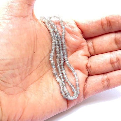 A person holds delicate strands of Labradorite beads, showcasing their smooth design.