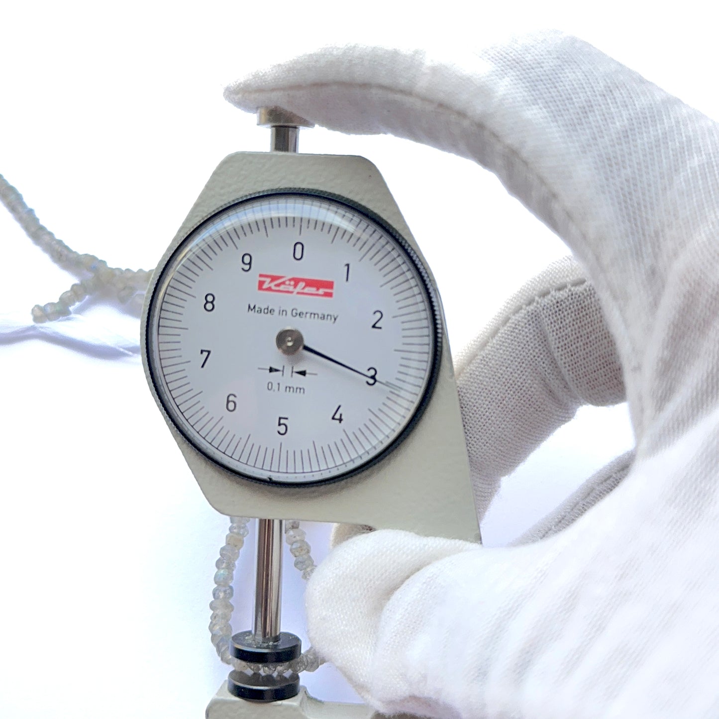 A dial gauge measures the Labradorite faceted rondelle 3.1–3.3mm gemstone.