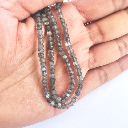 A person holds delicate strands of Labradorite beads, showcasing their colour play.