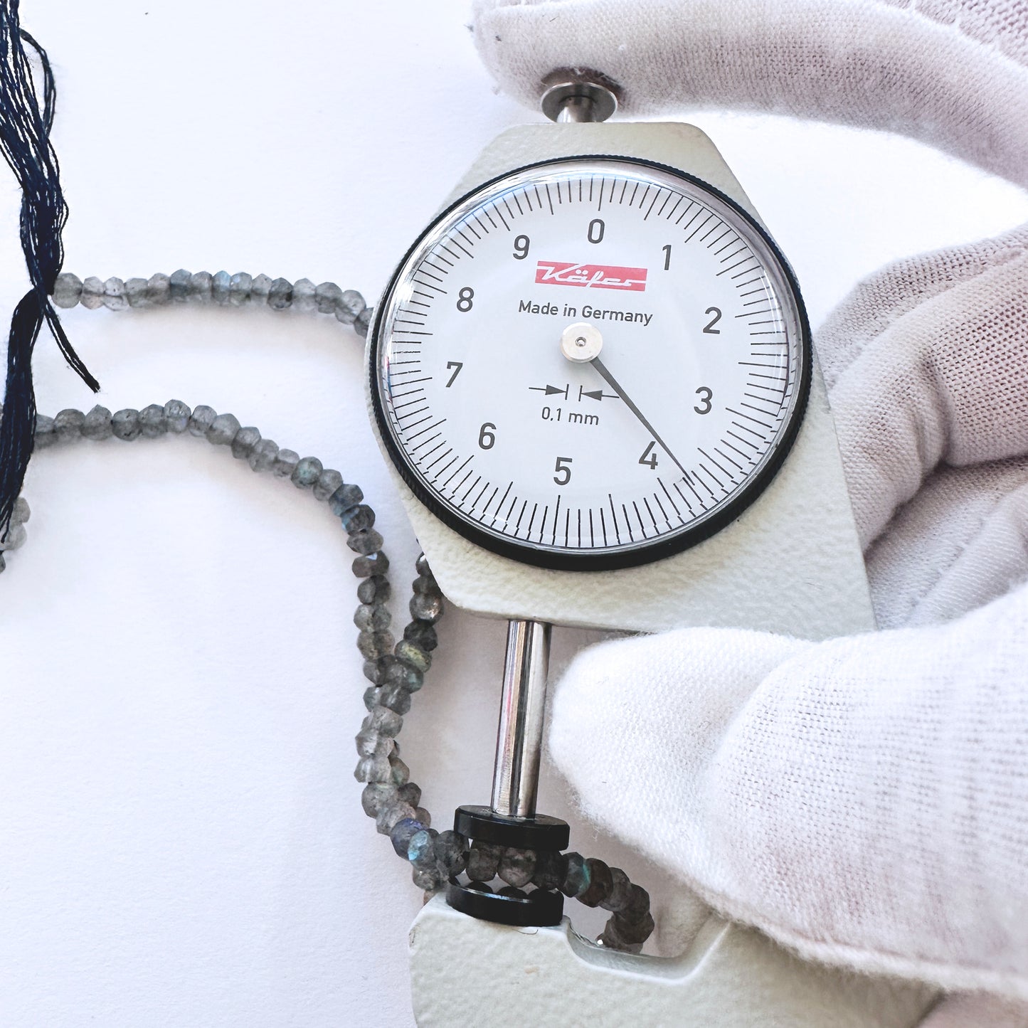 A dial gauge measures the Labradorite faceted rondelle 3.7-4.1mm gemstone.