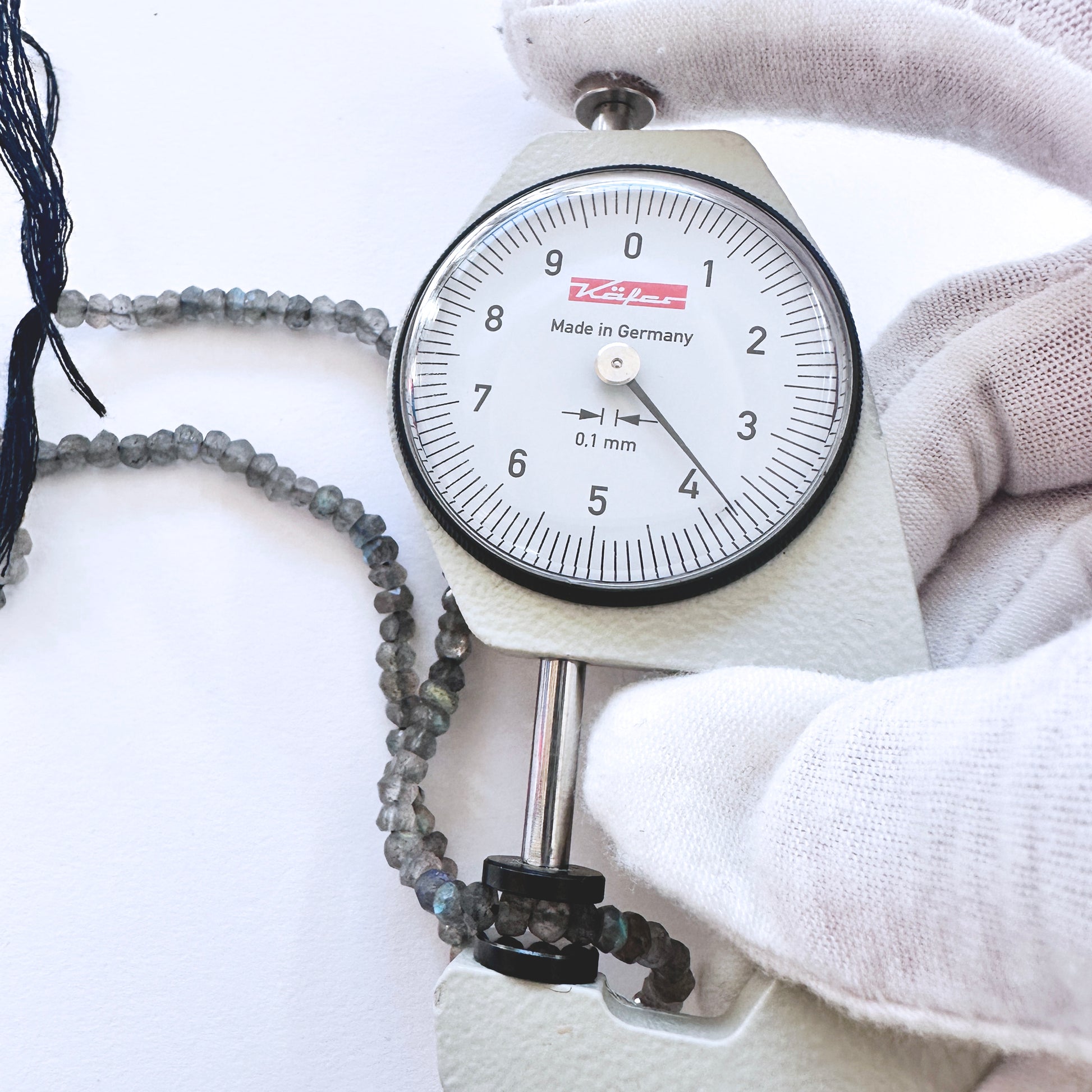 A dial gauge measures the Labradorite faceted rondelle 3.7-4.1mm gemstone.