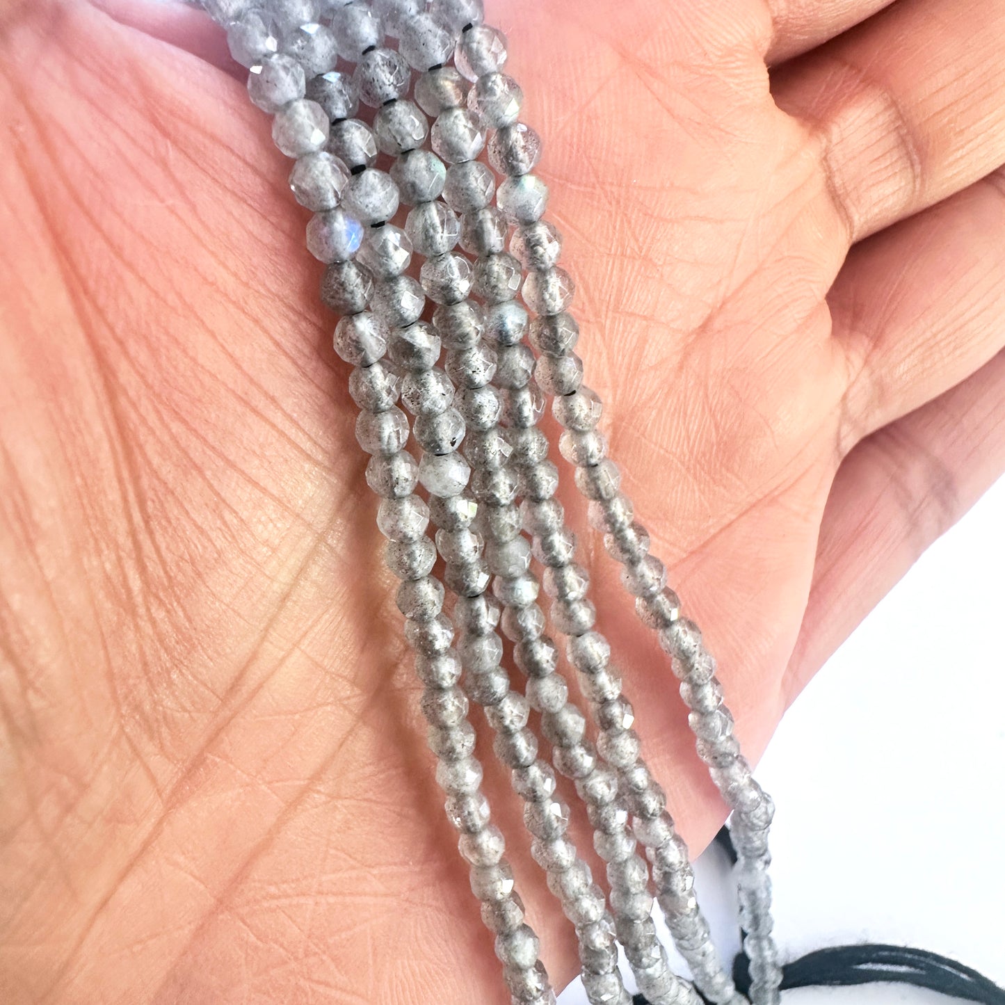 A person holds delicate strands of Labradorite beads, showcasing their smooth design.