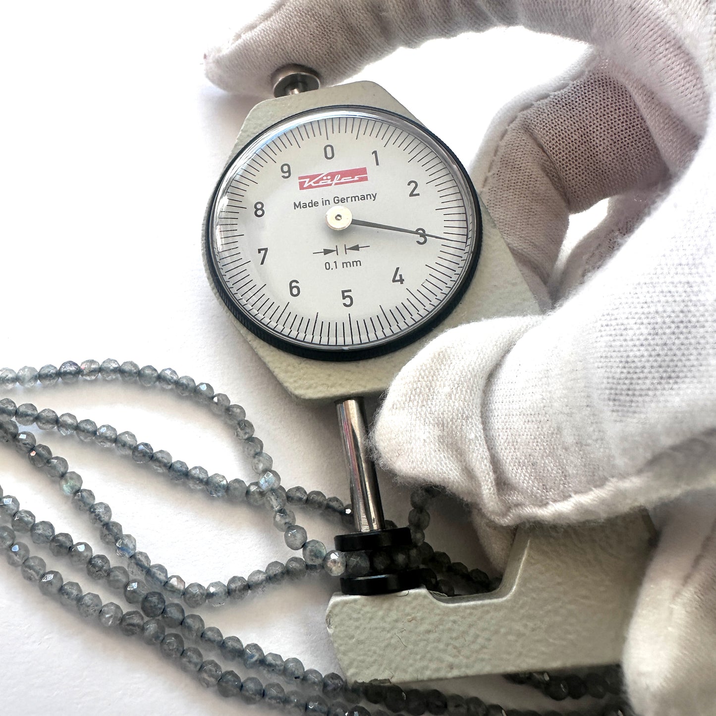A dial gauge measures the Labradorite faceted rondelle 3mm gemstone.