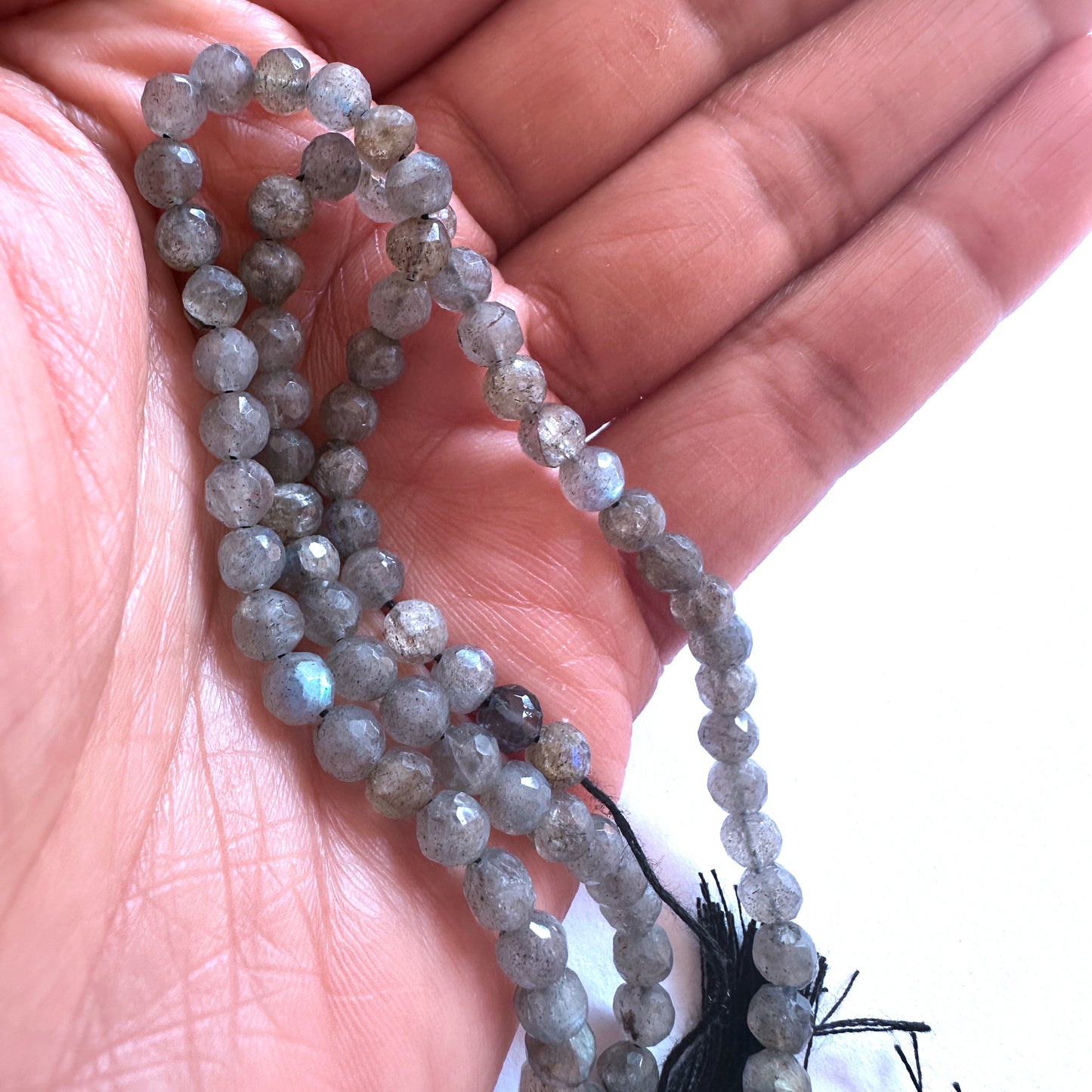 A person holds delicate strands of Labradorite beads, showcasing their smooth design.