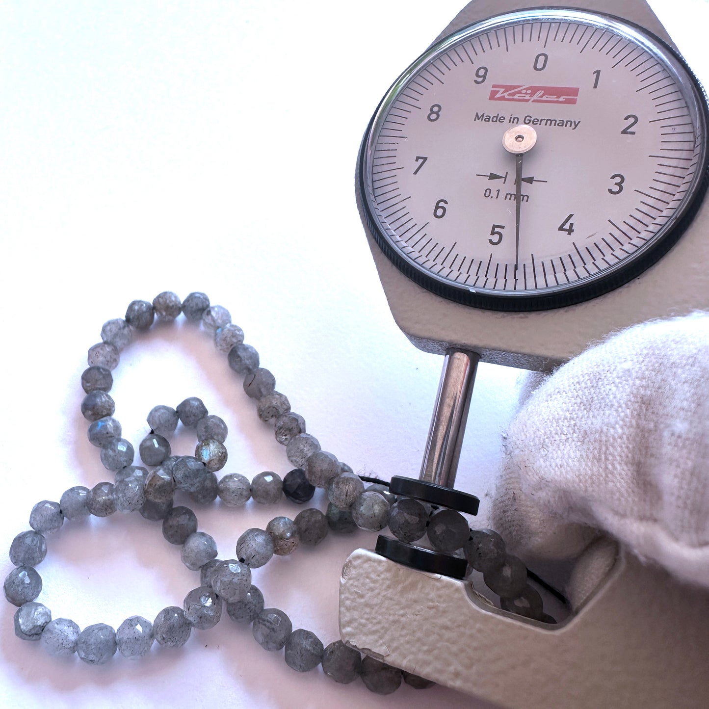 A dial gauge measures the Labradorite faceted rondelle gemstone.