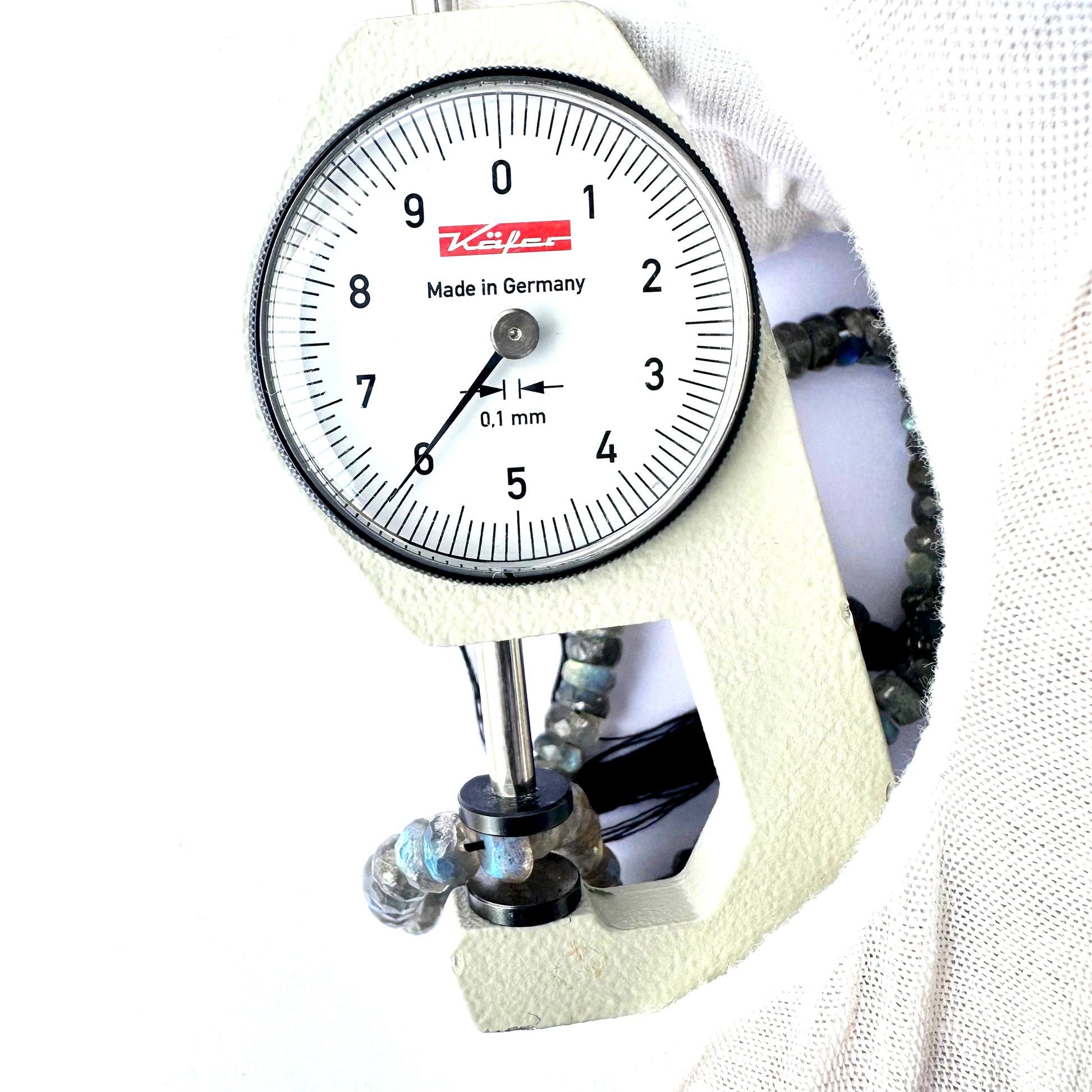 A dial gauge measures the Labradorite faceted rondelle 6.3-6.5mm gemstone.