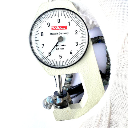 A dial gauge measures the Labradorite faceted rondelle 6.3-6.5mm gemstone.
