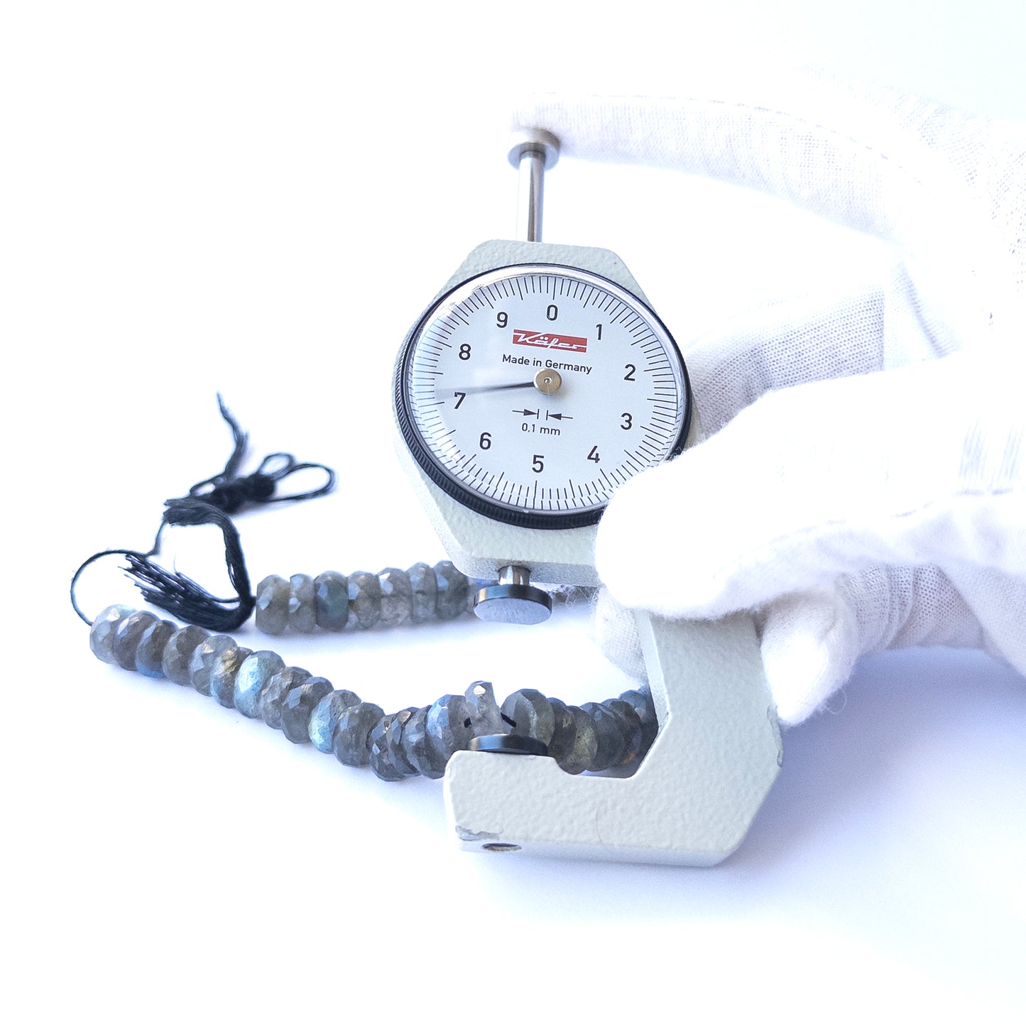 A dial gauge measures the Labradorite Faceted Rondelle 8.5–9mm gemstone.