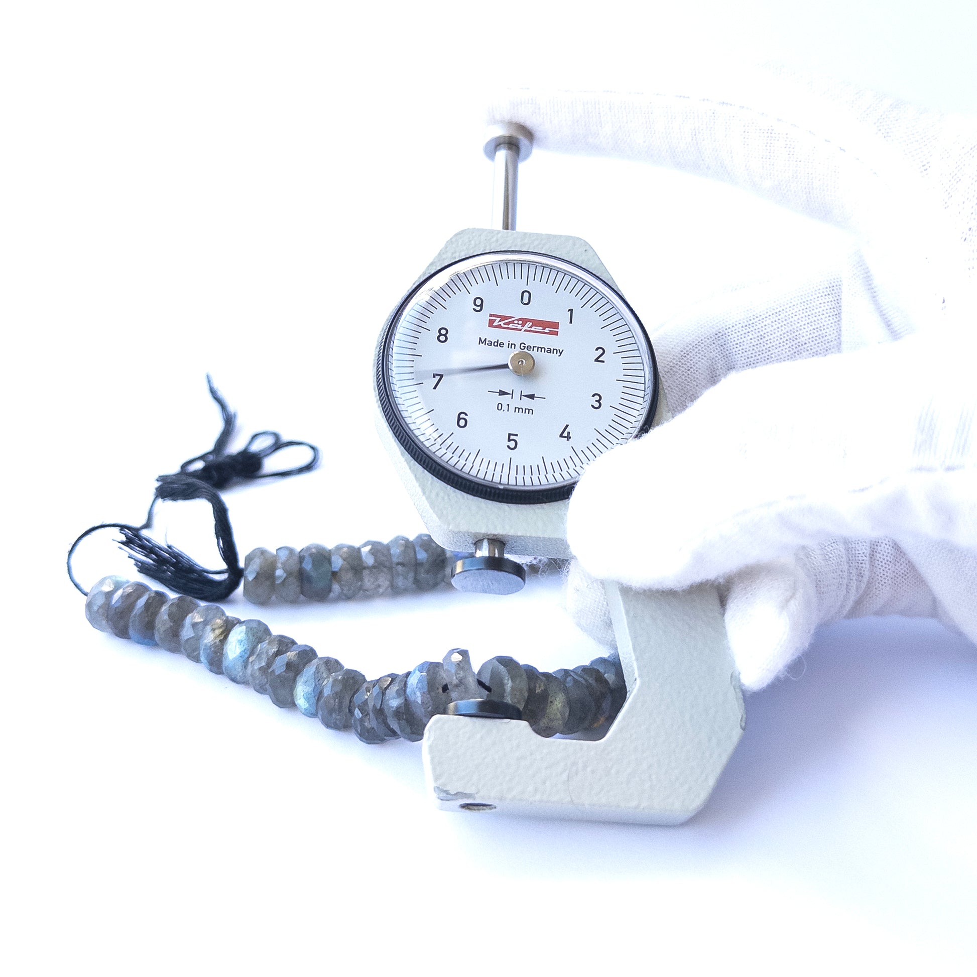 A dial gauge measures the Labradorite Faceted Rondelle 8.5–9mm gemstone.