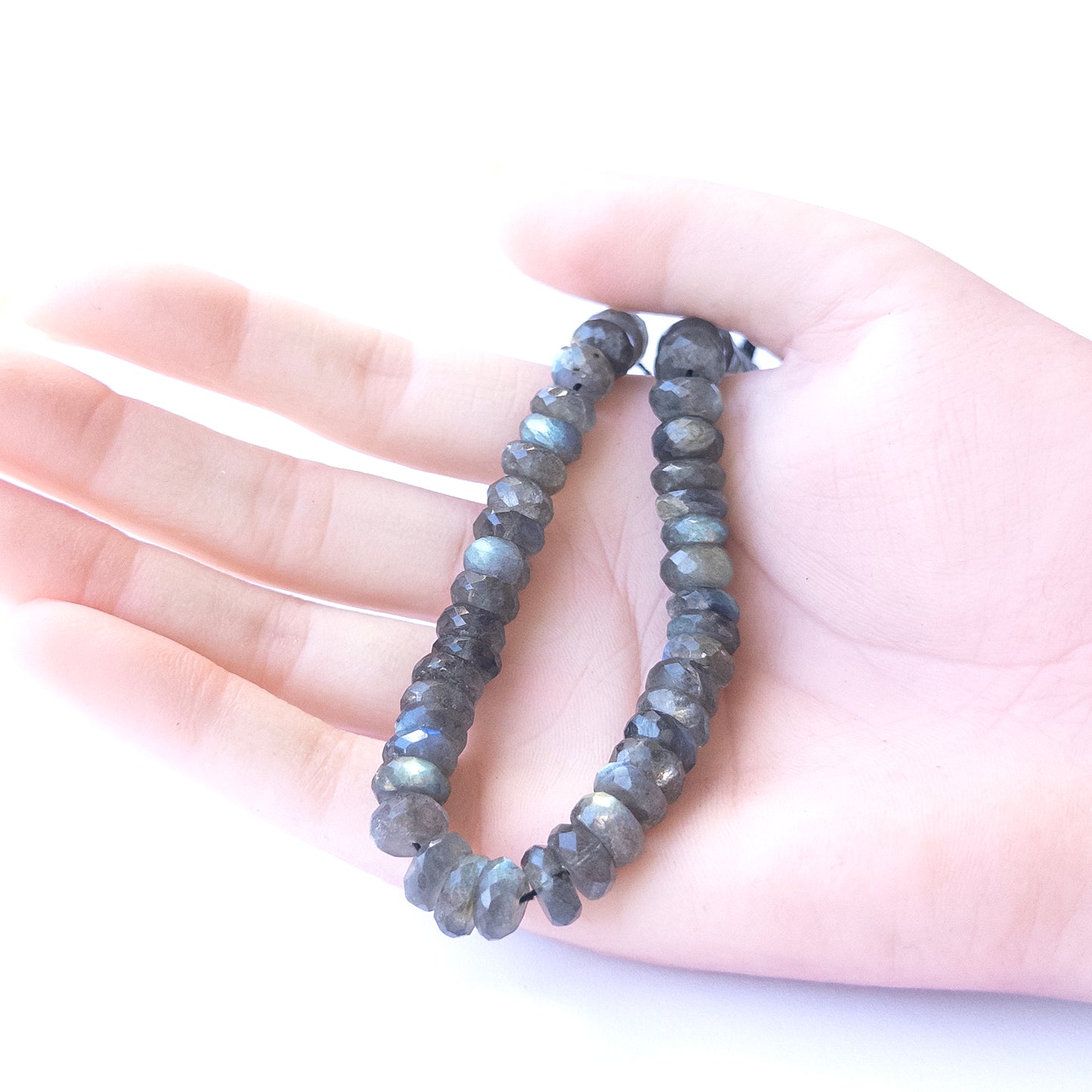 A person holds delicate strands of Labradorite beads, showcasing their Faceted Rondelle design.